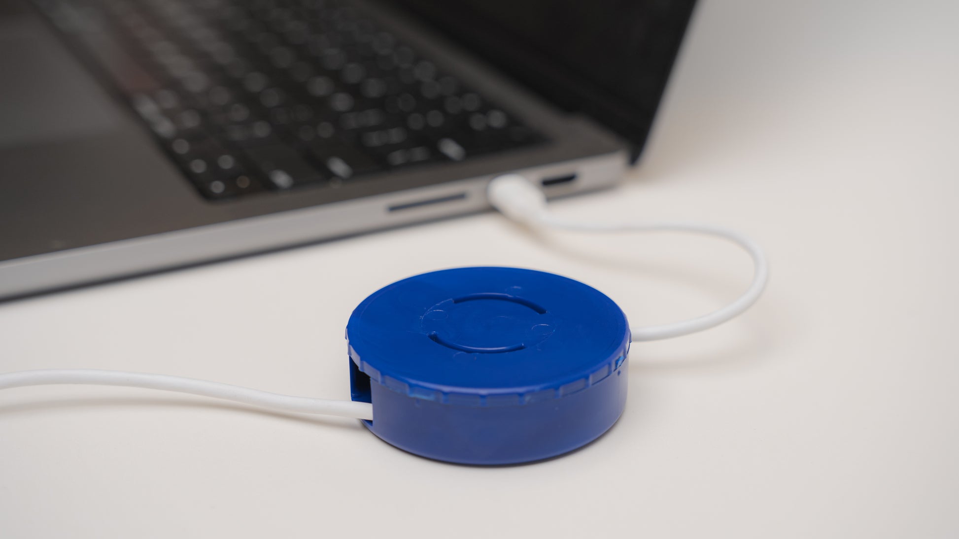 CordPuck cord organizer is holding and storing a charger cord while plugged into an Apple MacBook Air
